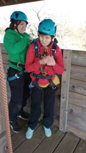 A learner is supported into a safety harness, ready to take on a rope obstacle