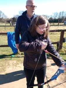 A young lady preparing a bow and arrow with support from a man