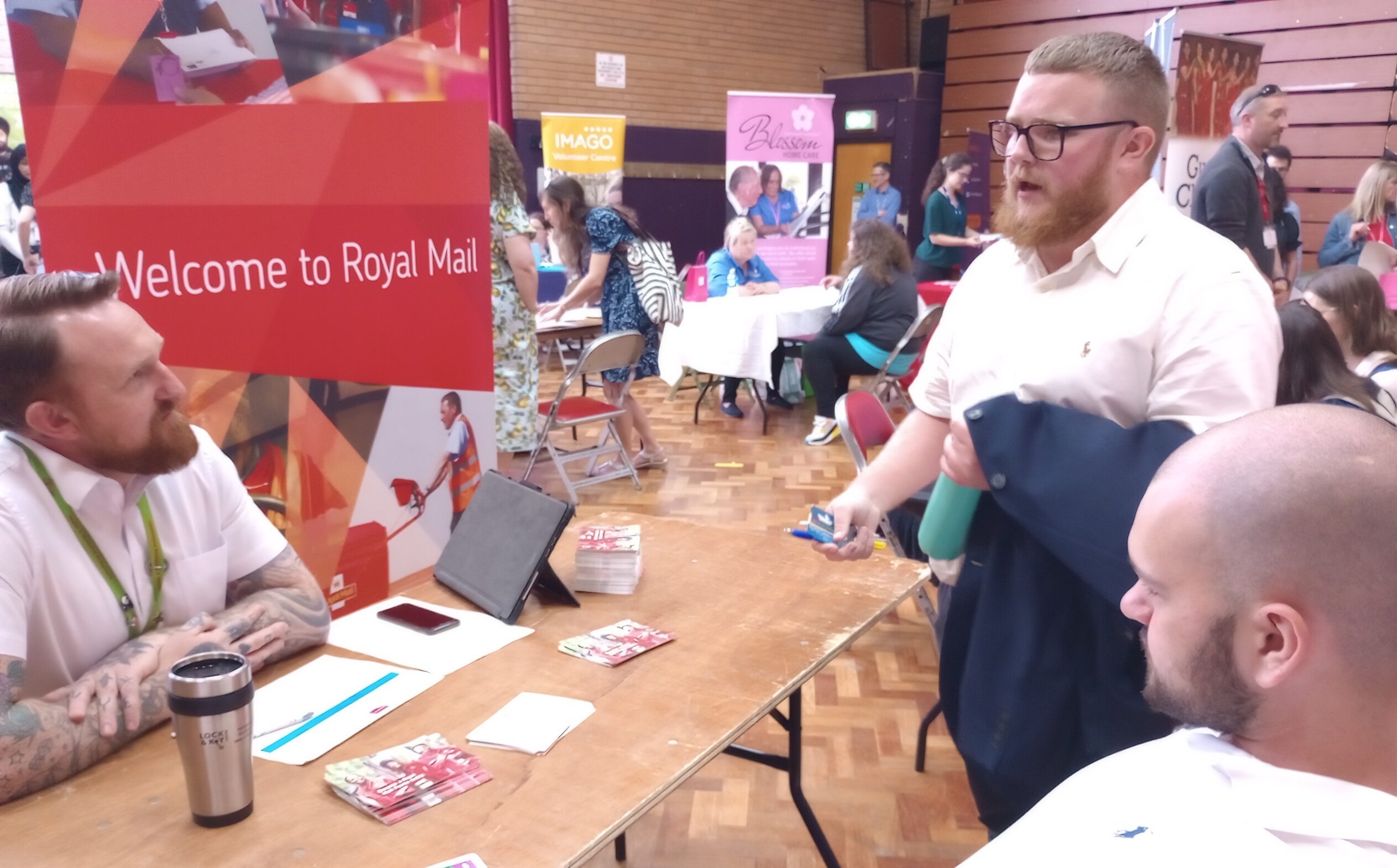 Two young men, speaking with a businessman at a busy jobs fair