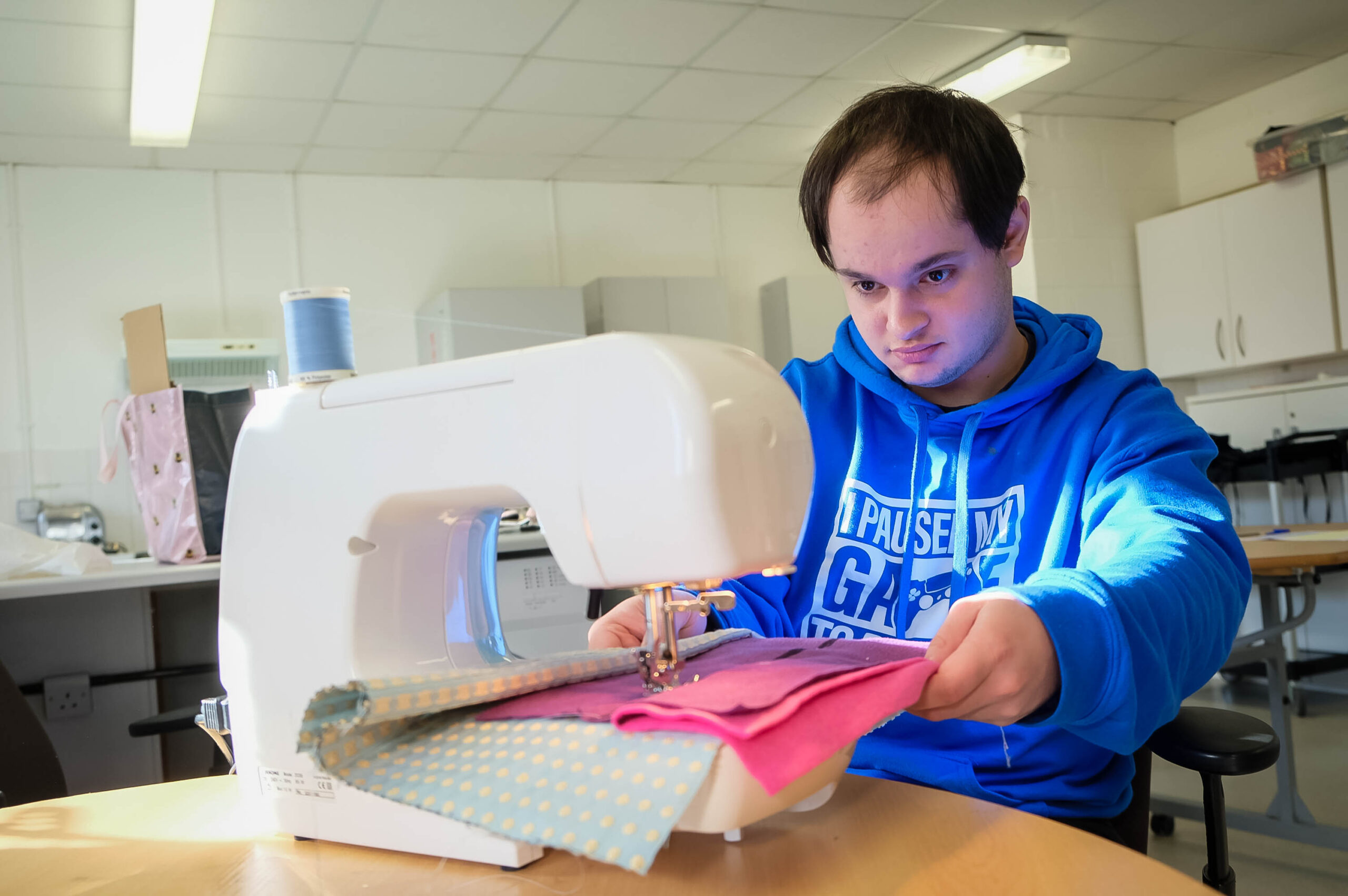 A young man, concentrating while stitching some bright pink on an electric sewing machine