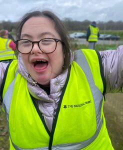 A young lady in National Trust branded hi-vis vest, laughing as she enjoys her volunteering role.