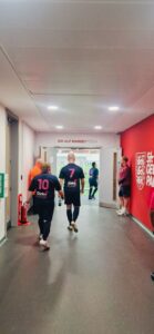 Several young men, dressed in full football kit, walk down the England Football Team's training academy tunnel, with their backs to the camera