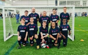 A football team, in an all navy blue kit, pose for a traditional football team photo in two rows. 
