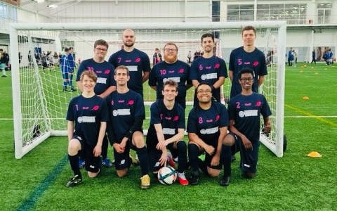 A football team, in an all navy blue kit, pose for a traditional football team photo in two rows.