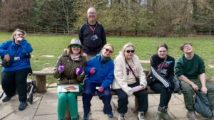 A group of young people, with their teacher, enjoying a lunch at some picnic tables