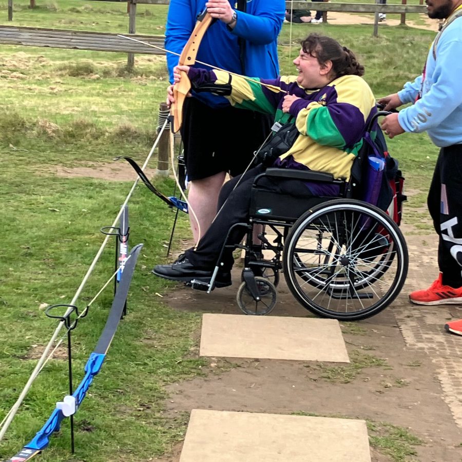 A young lady in a wheelchair being helped to aim a bow