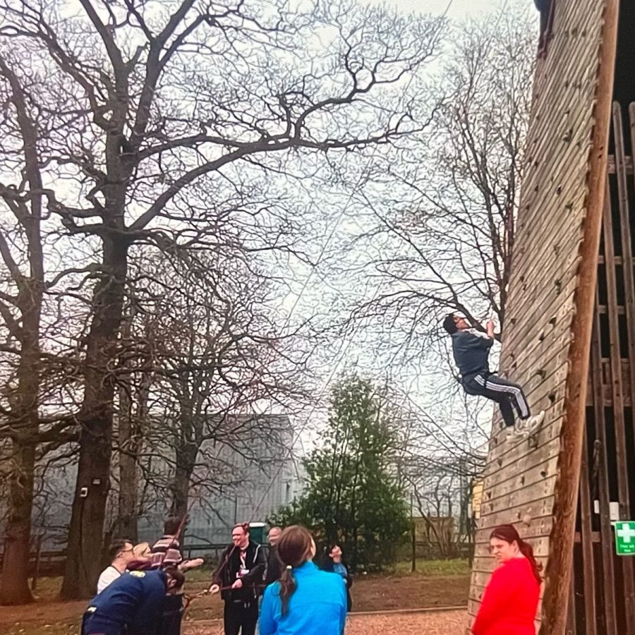 A person climbing an abseiling wall and a group watching him